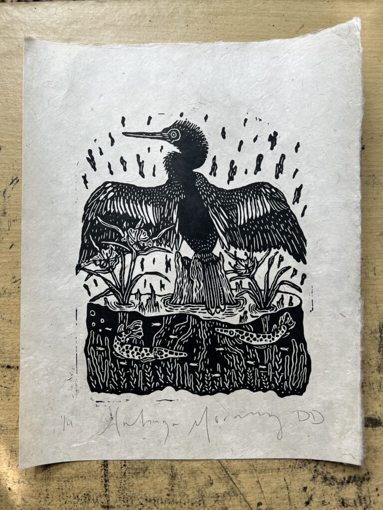 A black-and-white block print titled "Anhinga Morning." A water bird with spread wings sits on a stump above a water line. Below the surface, two spotted fish swim among aquatic plants. The print is on textured paper with pencil signatures at the bottom.
