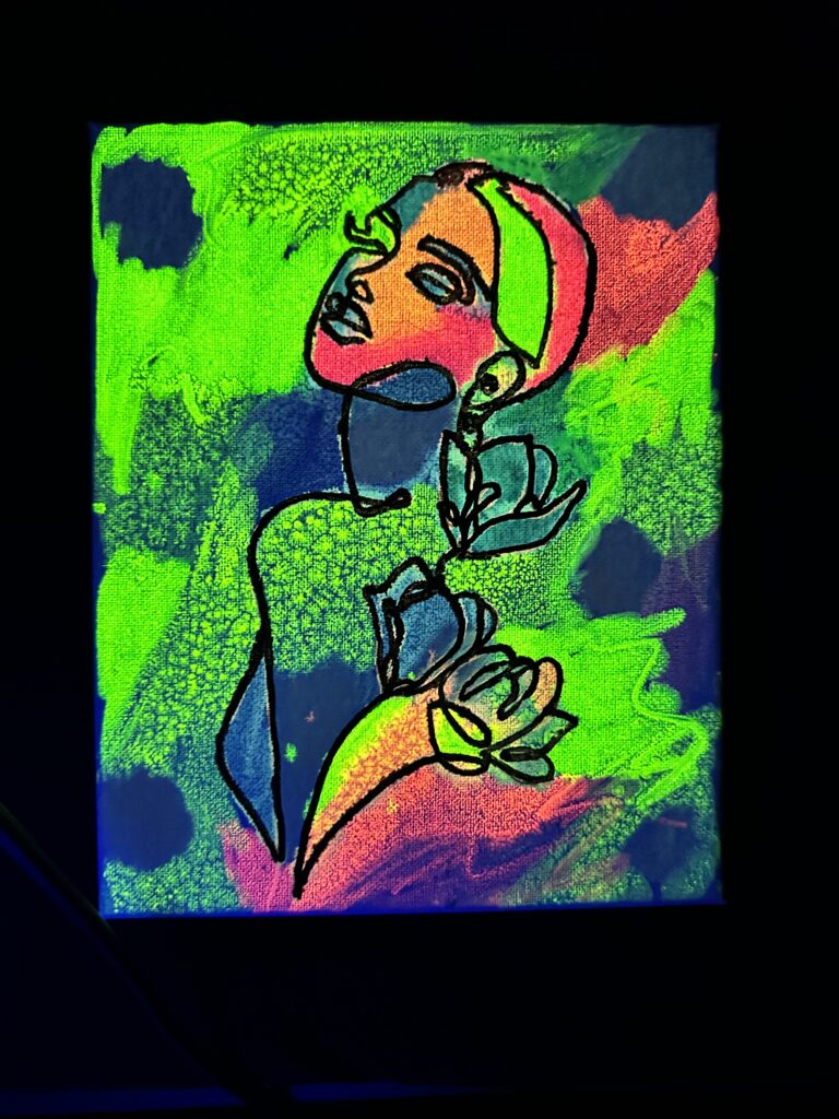 A vertical neon painting on a textured canvas featuring a continuous black line drawing of a person’s profile and torso. The figure is shown from the side, looking upward, with three stylized flowers blooming from their chest. The background is vibrant green, blue, and pink splatters that glow against a dark setting.